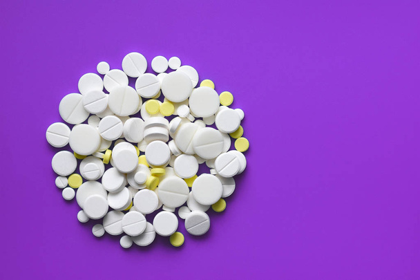 Žluté a bílé tablety roztroušených na fialový lékařský stůl, pozadí, kopírování prostor - Fotografie, Obrázek