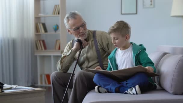 Boy reading book aloud, happy grandfather listening, stroking grandson head - 映像、動画
