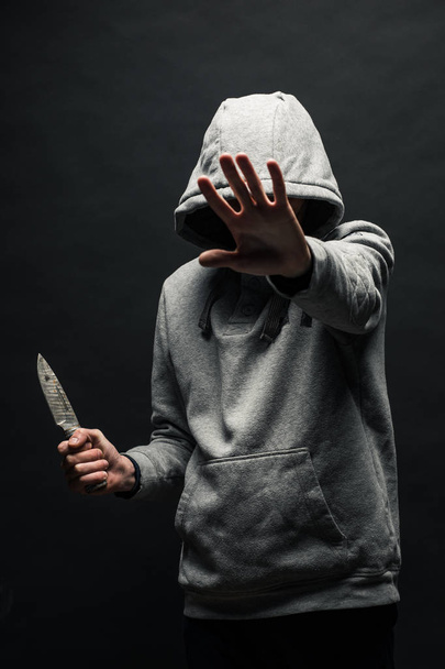 Опасный человек в капюшоне стоит в темноте и держит нож. Лицо не видно. Понятие преступления, убийства
. - Фото, изображение