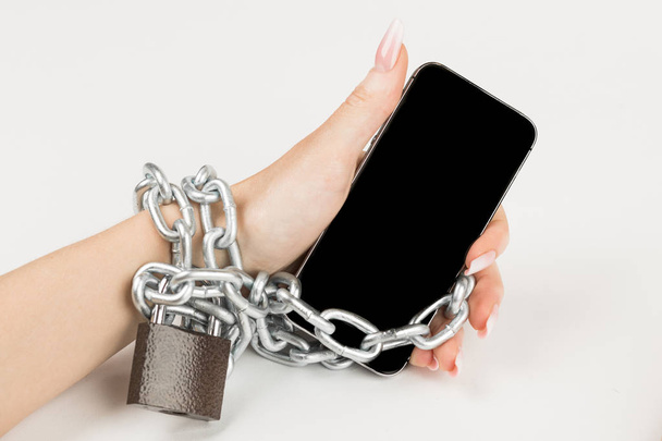 Żelazny łańcuch z zamkiem łączy razem ręka i smartphone. koncepcję uzależnienia od telefonu komórkowego. - Zdjęcie, obraz