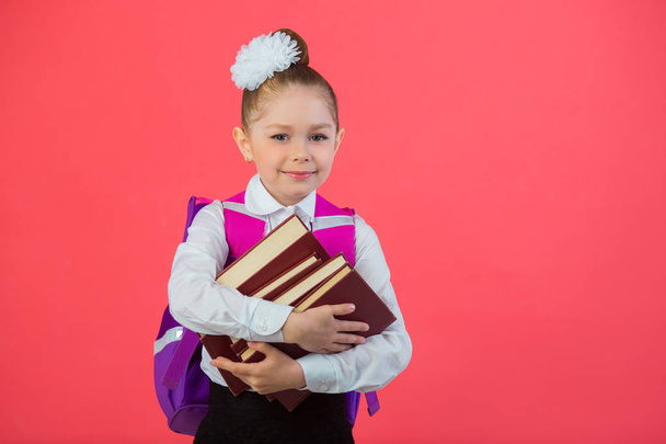 beautiful little girl with a bow with a school satchel on a pink background with a book in hands - Photo, Image