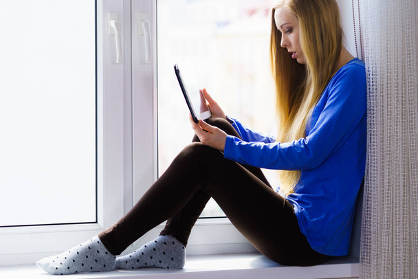Modern technology education internet, digital online learning concept. Long hair teen girl with tablet pc computer on window sill - Фото, изображение