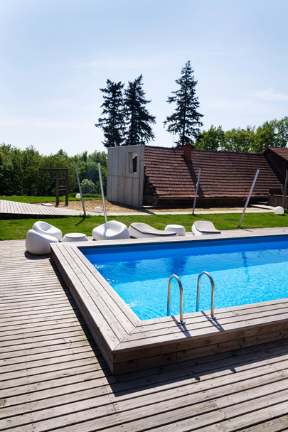 Mooie buiten skimmer zwembad met houten vloeren en inox ladder trap, zonnige zomerdag, kopie ruimte - Foto, afbeelding