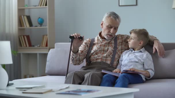 Grandpa watching photo album with grandson, remembering youth, telling stories - Кадри, відео