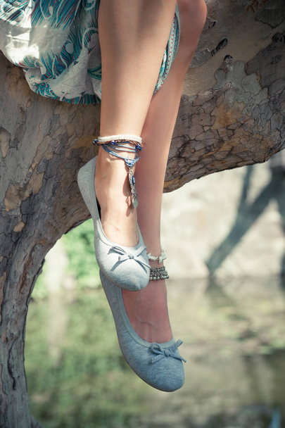 jambes de femme assis sur l'arbre dans le parc avec des bracelets de cheville portant des chaussures d'été plat clair gros plan
 - Photo, image