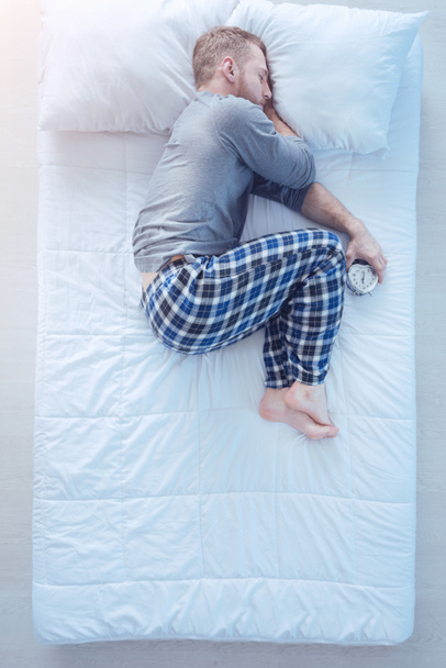 Man with alarm clock sleeping in fetal position - Zdjęcie, obraz