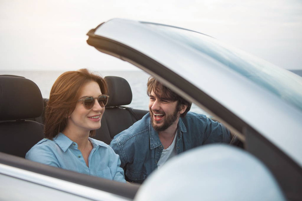 Lets go there. Cheerful romantic man is driving car with open roof while his girlfriend is sitting near him. They are travelling together while enjoying romantic vacation abroad. Relationship concept - Фото, изображение