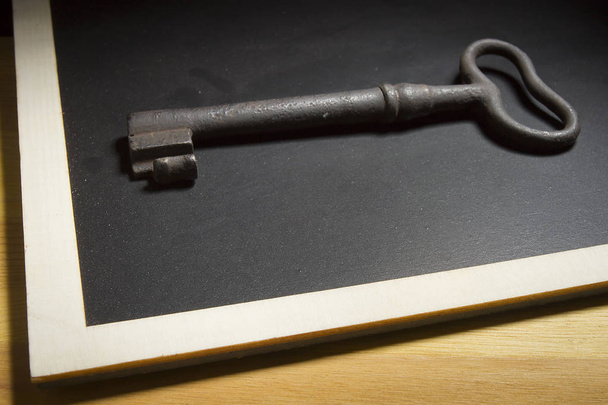 Old rusty key on a black slate - Foto, imagen