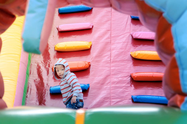 a little boy plays in a colorful children's trampoline complex on the playground - Foto, Imagen