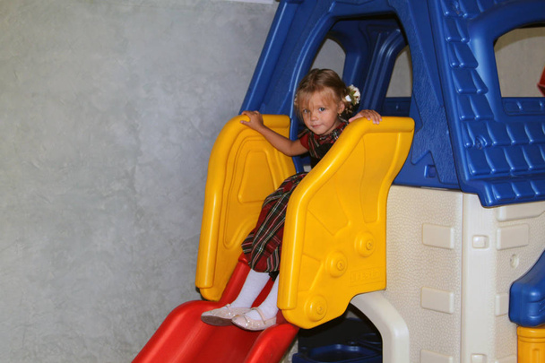 little girl in a plaid dress with riding the slide in kindergarten - Zdjęcie, obraz