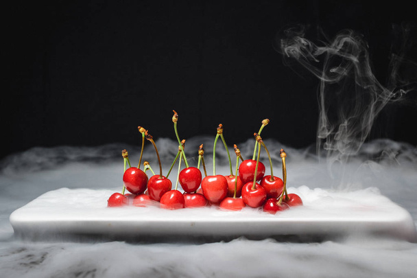 Fresh cherries lie on ice on a black background and soar. close up - 写真・画像