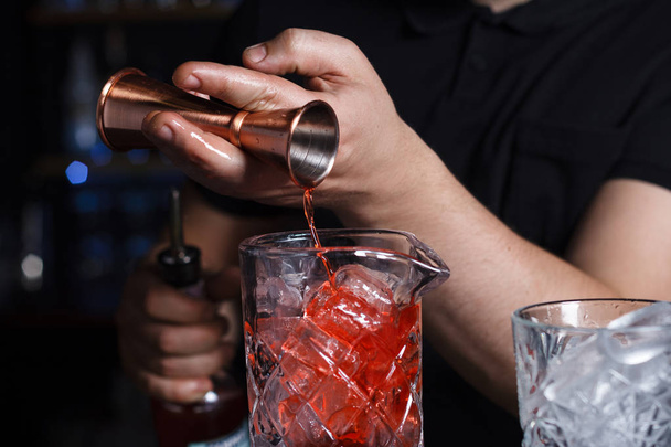 Barman mixologist is alcohol gieten van een jigger in een meetinstrument glas over ijs. Close-up. - Foto, afbeelding