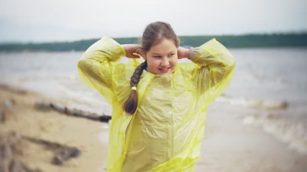 Gelukkig meisje wandelen langs de kust Lifestyle reizen avontuurlijke vakantie buitenshuis. Een meisje gekleed in een modieuze gele regenjas - Video