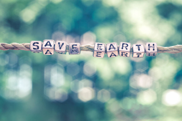 Save Earth word hanging by rope with beautiful green nature bokeh background with vintage retro tone. - Valokuva, kuva