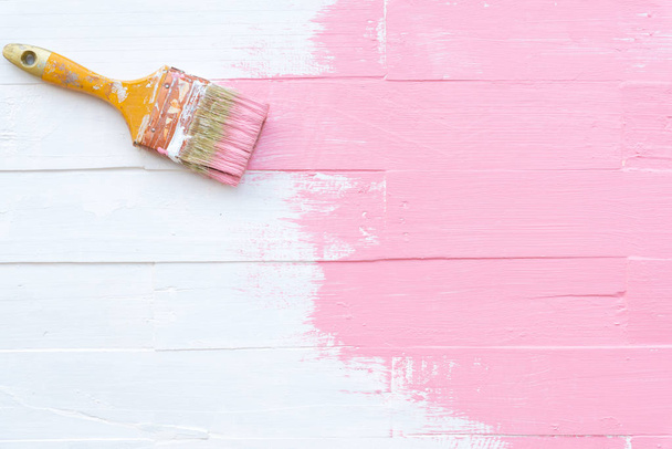 Pinsel in Nahaufnahme pinselt rosa Farbe auf einen weißen Holztisch - Foto, Bild