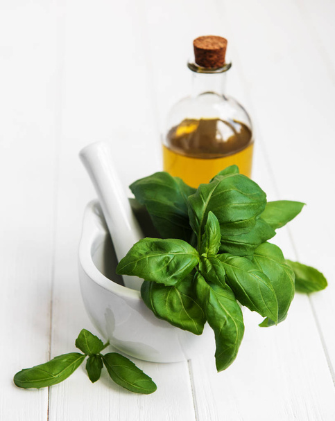 Tuore vihreä basilika ja oliiviöljy valkoisella puupöydällä
 - Valokuva, kuva