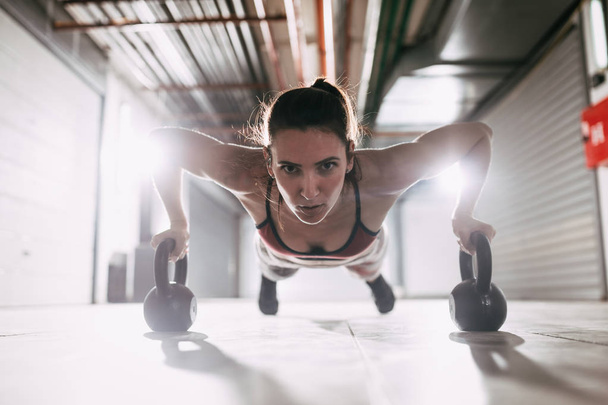 Молодая мускулистая женщина делает упражнения с гирями на тяжелых тренировках
 - Фото, изображение