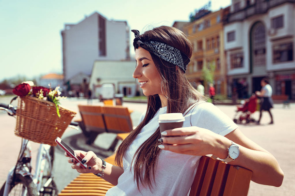 mladá žena s kolo s květinový koš pomocí smartphone a pití kávy - Fotografie, Obrázek