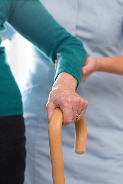 Femmes âgées mains sur bâton de marche avec travailleur de soins en arrière-plan
 - Photo, image