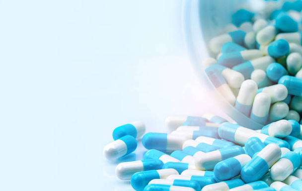 blaue und weiße Kapseln Pille aus weißen Plastikflaschenbehältern verschüttet. globales Gesundheitskonzept. Antibiotika-Resistenz. Antimikrobielle Kapselpillen. Pharmaindustrie. - Foto, Bild