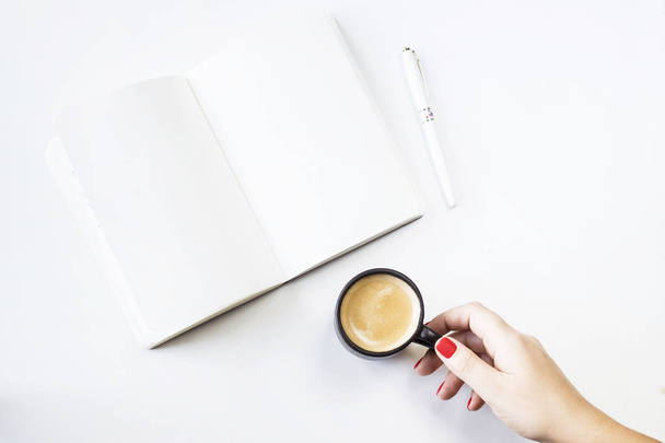 Ανοίξτε το σημειωματάριο ένα λευκό καθαρό φύλλα δίπλα σε ένα λευκό στυλό και ένα φλιτζάνι καφέ στα γυναικεία χέρια. Έννοια του μινιμαλισμού και της δημιουργικότητας - Φωτογραφία, εικόνα