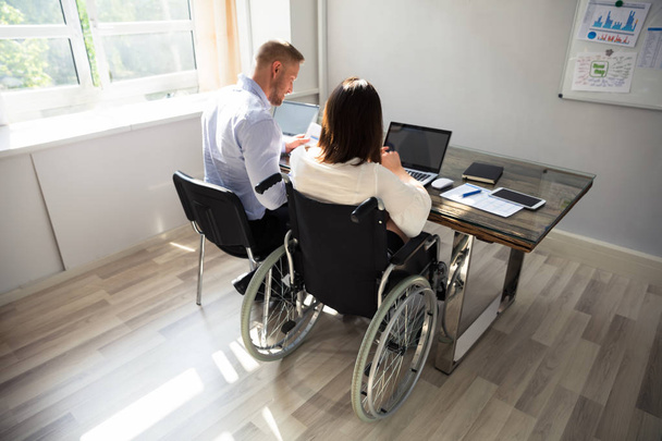 Disabled Businesswoman Sitting With Her Partner With Laptop Over Desk In Office - Zdjęcie, obraz