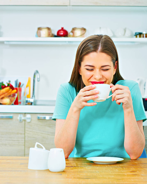 laughing casual dressed woman drinking coffee in kitchen at home - Фото, изображение