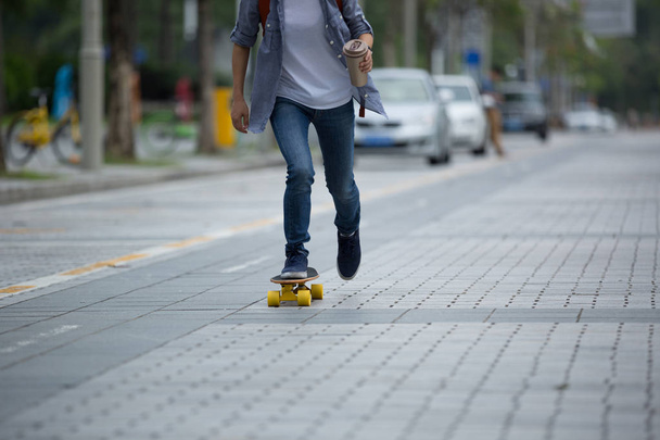 woman skateboarding with coffee cup in hand on city street - Photo, Image