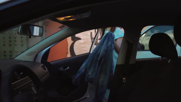 Woman put a jacket on the car seat and sits down on the drivers seat, intending to start the engine - Πλάνα, βίντεο