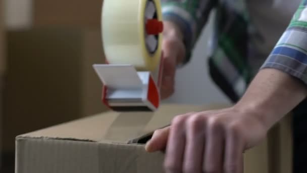 Man packing cardboard box with adhesive tape, moving out, migration, life change - Filmagem, Vídeo