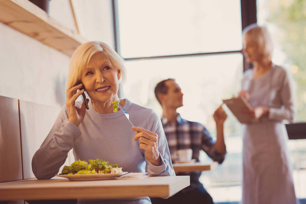 Pleasant woman enjoying salad and talking on phone - Fotografie, Obrázek