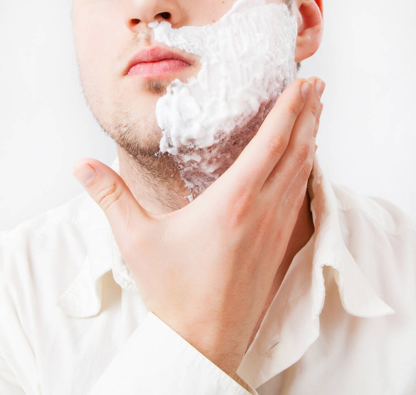 Young man with foam shaving his beard off with an electric shaver - Photo, Image