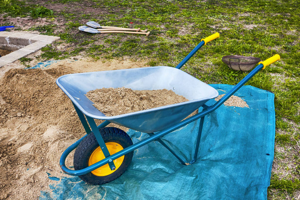 Blauwe en gele kruiwagen voor het vervoer van zand of zware materialen - Foto, afbeelding