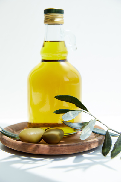 bouteille avec huile aromatique aux olives vertes sur panneau de bois avec branche sur table blanche
 - Photo, image
