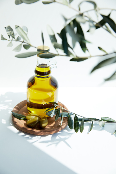 bouteille d'huile aromatique aux olives vertes sur planche de bois et branches sur table blanche
 - Photo, image