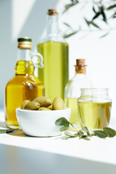 diverses bouteilles d'huile d'olive aromatique, pot, bol aux olives vertes et branches sur table blanche
 - Photo, image