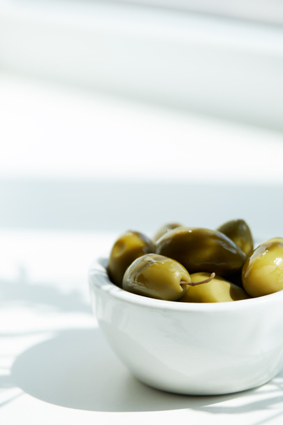 lähikuva kulhoon vihreitä oliiveja valkoisella pöydällä
 - Valokuva, kuva