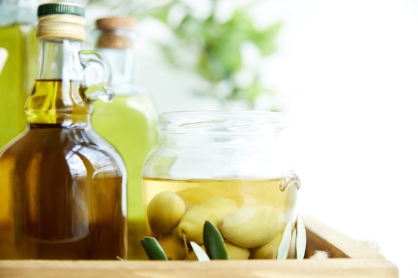 gros plan du pot aux olives vertes, bouteilles d'huile d'olive aromatique et branches sur plateau en bois
 - Photo, image