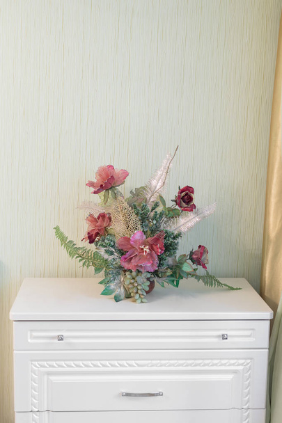 Flores artificiales en una cómoda costosa
 - Foto, imagen