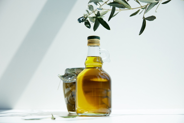 láhev z aromatických olivový olej, poboček a jar se zelenými olivami na bílém stole - Fotografie, Obrázek