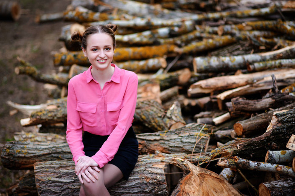 Belle jeune femme assise sur une pile de troncs d'arbres abattus dans la forêt
. - Photo, image