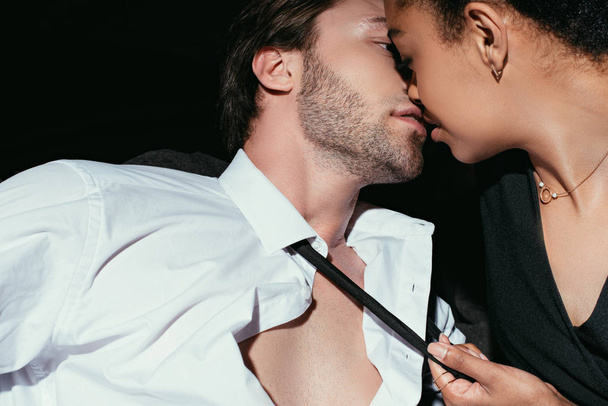 junge multirassische sexy Paar in schwarzer Kleidung küssen auf dunklem Hintergrund - Foto, Bild