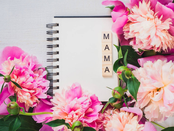 Blank page of the notebook with the word MAMA for the greeting inscription on the background of flowering flowers. Top view, closeup, isolated. Congratulations to relatives. Concept of a happy family - 写真・画像