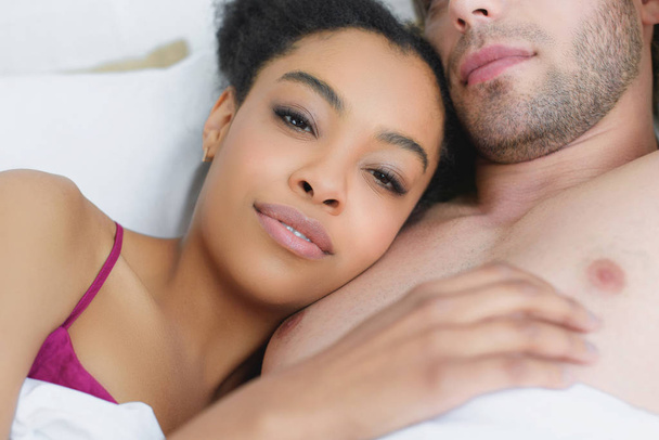 partial view of multiethnic young couple in love lying in bed together in morning - Foto, Imagem