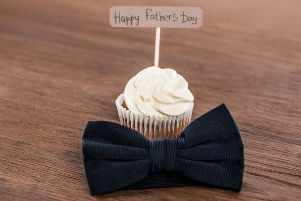 lekkere cupcake met bowtie en gelukkig vaders dag inscriptie op houten oppervlak - Foto, afbeelding