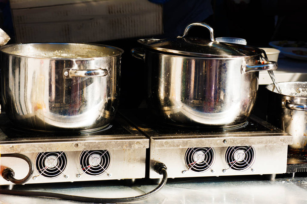 Dwa metalowe miski stanąć na kuchenka elektryczna. Przygotowując posiłek. - Zdjęcie, obraz