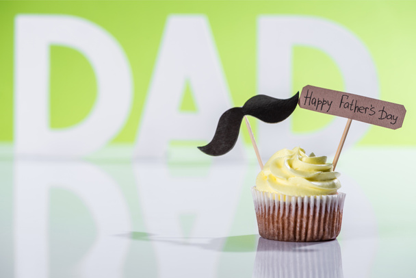 creamy cupcake with mustache sign and Happy fathers day inscription in front of dad inscription made of white letters on green - Photo, Image