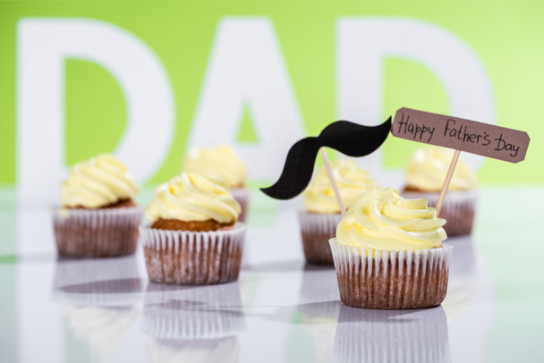 creamy cupcakes with mustache sign and Happy fathers day inscription in front of dad inscription made of white letters on green - Foto, afbeelding