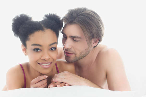 portrait of young interracial couple resting in bed together in morning at home - Fotó, kép