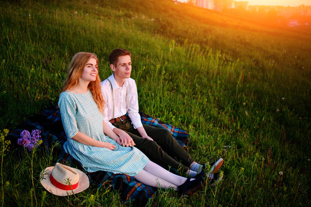 young couple sitting on the plaid in the park and look at the sunset. - Φωτογραφία, εικόνα